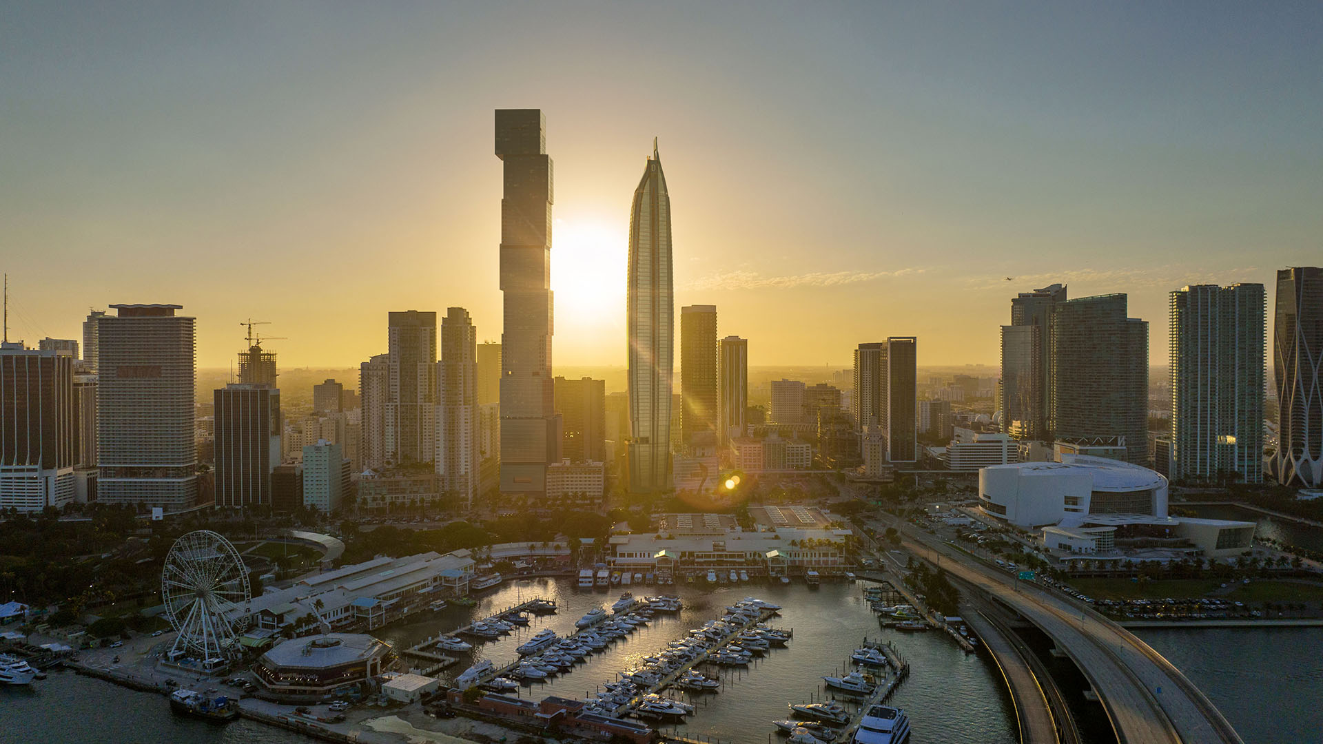 Aerial sunrise skyline view at Delano Residences & Hotel, Miami, with a marina, bridge, and surrounding high-rise towers, showing luxury and ultra luxury preconstruction condos on the waterfront.