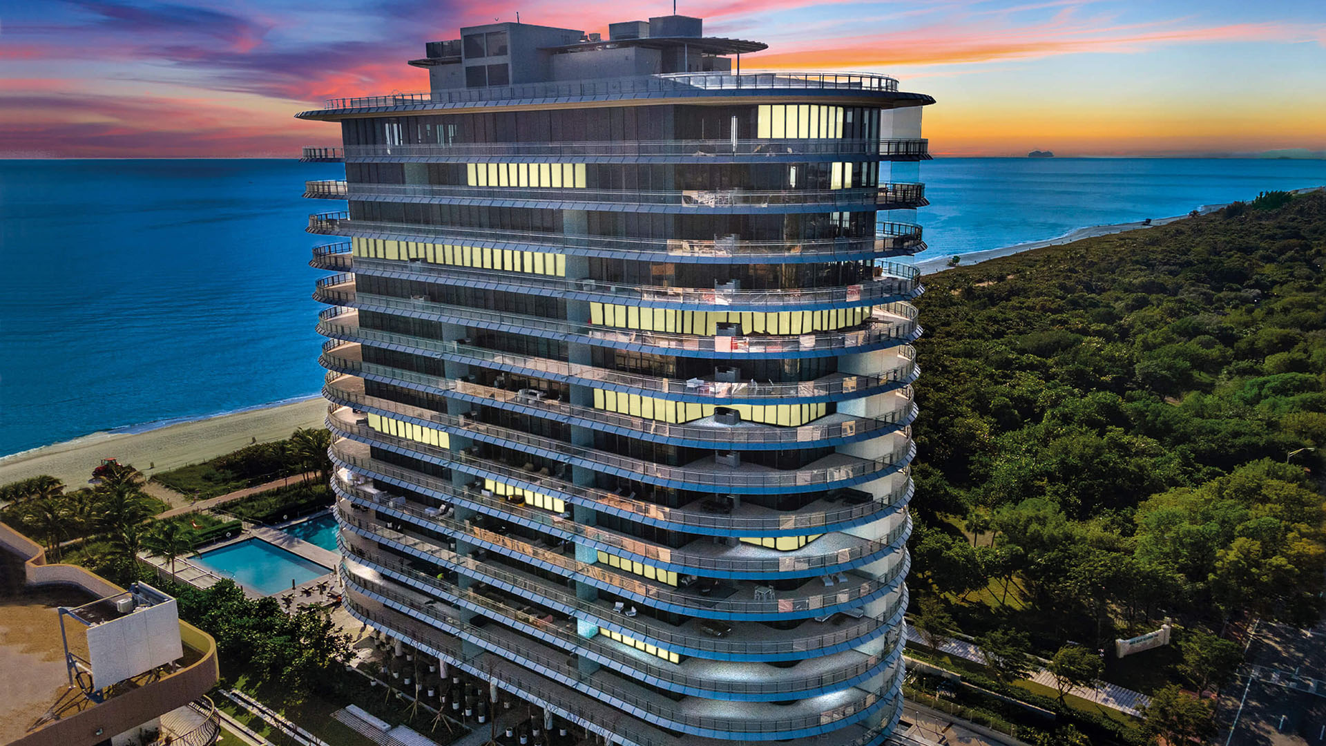 Eighty Seven Park, Miami Beach luxury and ultra luxury condos illuminated at sunset in an aerial view above the beach and ocean with colorful twilight sky.