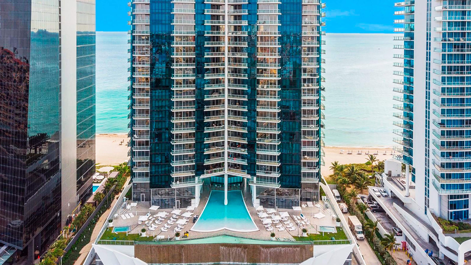 Oceanfront tower facade at Jade Ocean in Sunny Isles Beach, presenting luxury and ultra luxury condos above a dramatic podium pool deck with the beach and ocean directly behind the building.