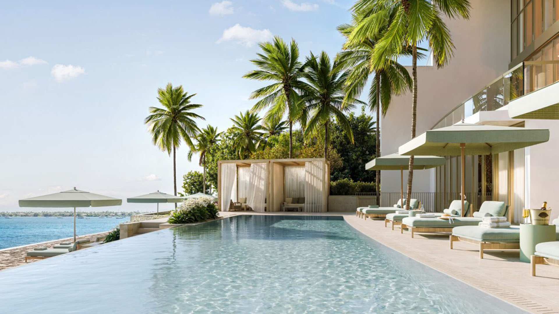 Long waterfront pool lined with loungers, palms, and a curtained cabana at Mandarin Oriental Residences, West Palm Beach, ultra luxury condos in West Palm Beach with a luxury outdoor amenity setting.