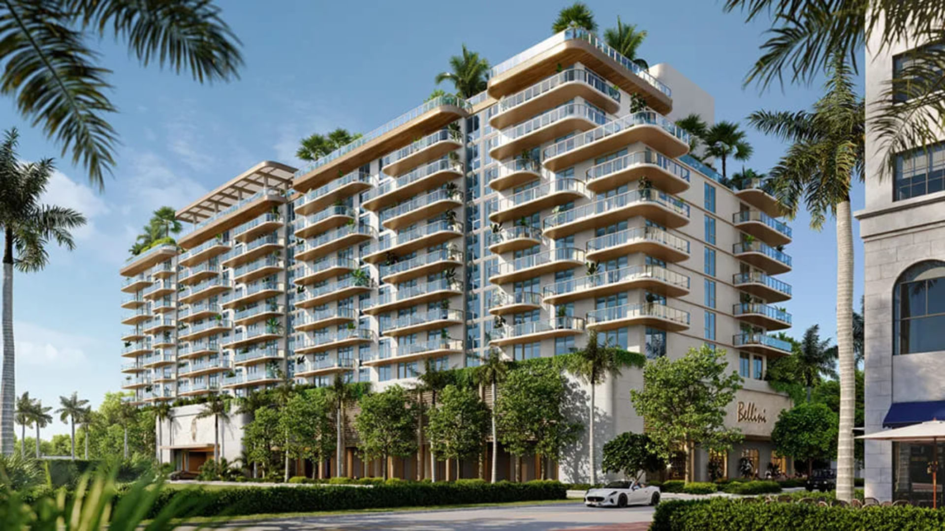 Curved condo exterior at Mr. C Residences in Boca Raton with wraparound glass balconies, rooftop greenery, and a palm-lined street scene, showcasing preconstruction luxury and ultra luxury condos.