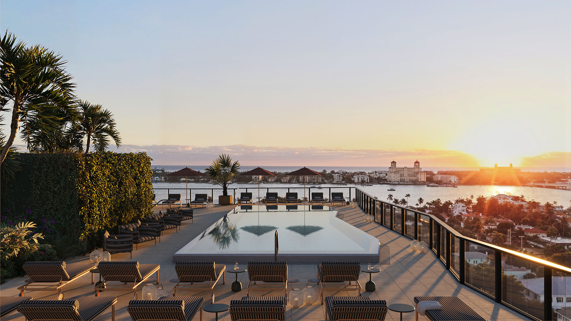Sunset rooftop pool terrace at Nora House in West Palm Beach, luxury and ultra luxury condos featuring a serene rooftop pool, striped loungers, glass railings, and sweeping waterfront views at golden hour.