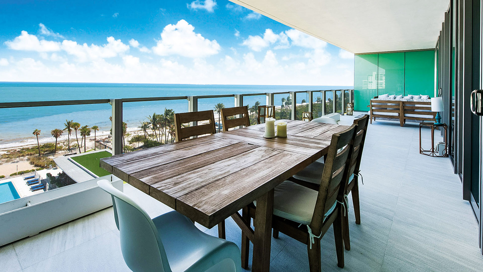 Beachfront dining terrace at Oceana Key Biscayne in Key Biscayne, showing luxury and ultra luxury condos with a long covered balcony, outdoor dining table, lounge seating, and sweeping ocean views.