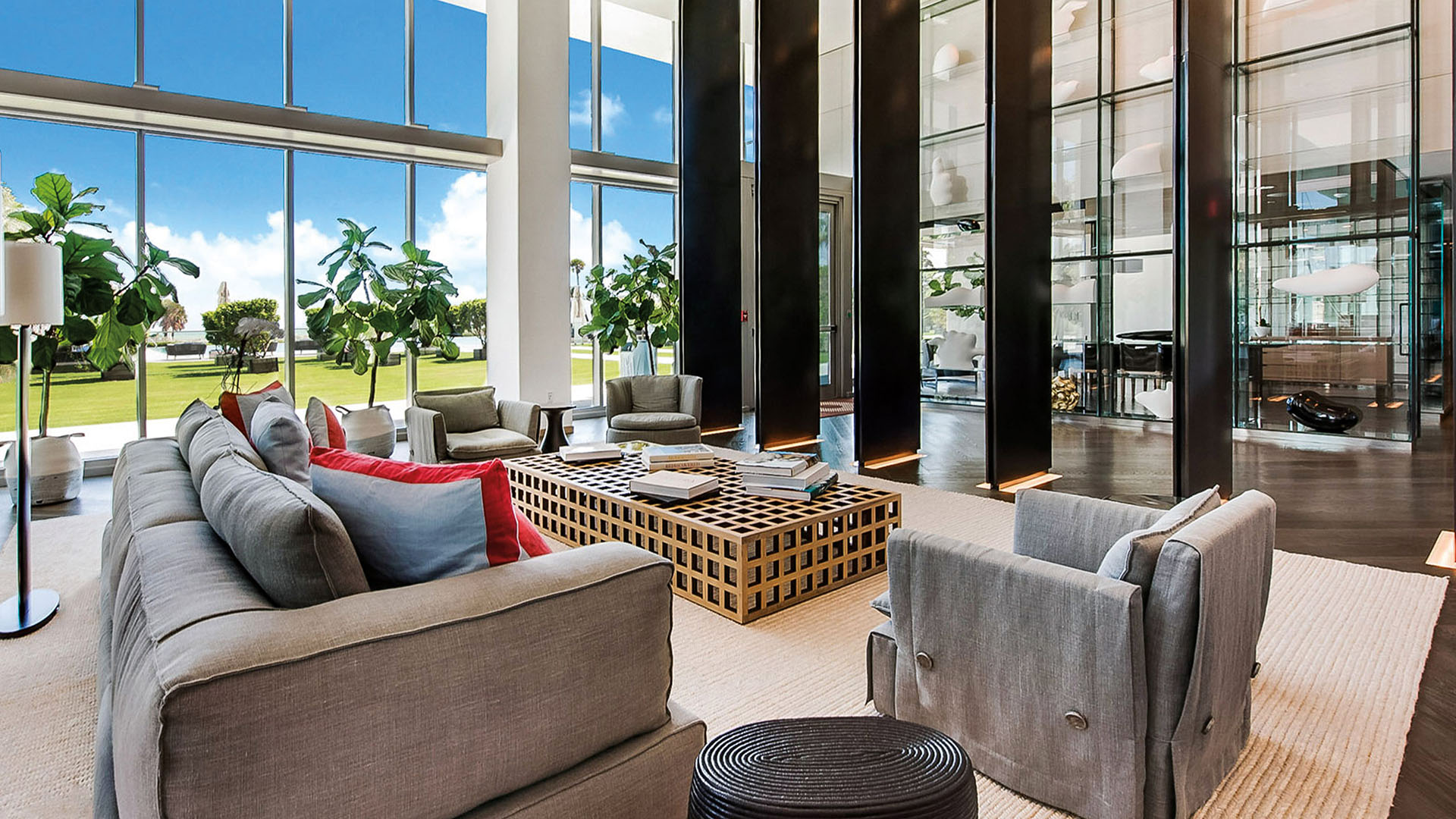Glass-walled lobby lounge at Oceana Key Biscayne in Key Biscayne, featuring luxury and ultra luxury condos with expansive windows, modern seating, display shelving, and landscaped views.
