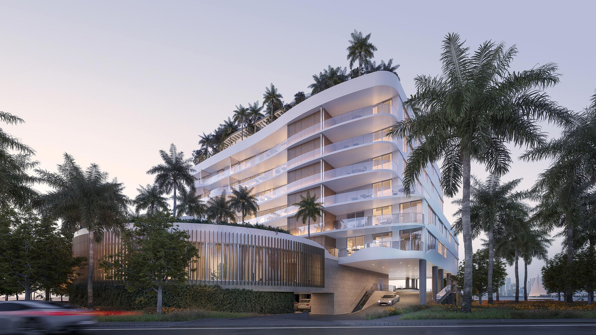 Onda Bay Harbor exterior street view at dusk in Bay Harbor Islands, Miami, Florida featuring curved modern architecture, balconies and palm-lined entrance-luxury and ultra luxury preconstruction condos.
