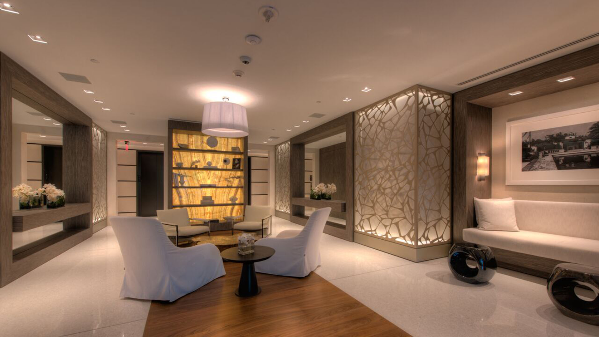Reception lobby at Palazzo del Sol, Fisher Island, reflecting luxury and ultra luxury condos with backlit display shelving, sculpted wall panels, lounge seating, and a polished contemporary arrival.