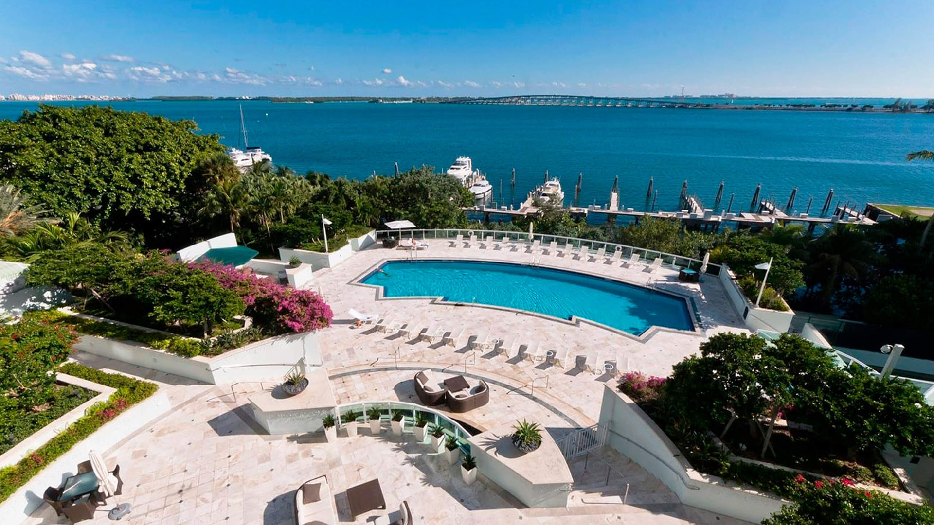 Waterfront pool deck and marina overlook at Santa Maria in Brickell, showing luxury and ultra luxury condos with landscaped grounds, lounge seating, docked yachts, and broad bay views.