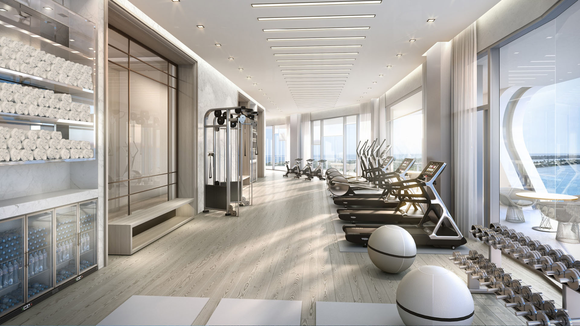 Sunlit fitness center with treadmills, weights, and full-height waterfront windows at The Bristol Palm Beach in Palm Beach, designed for luxury and ultra luxury condos living and wellness.
