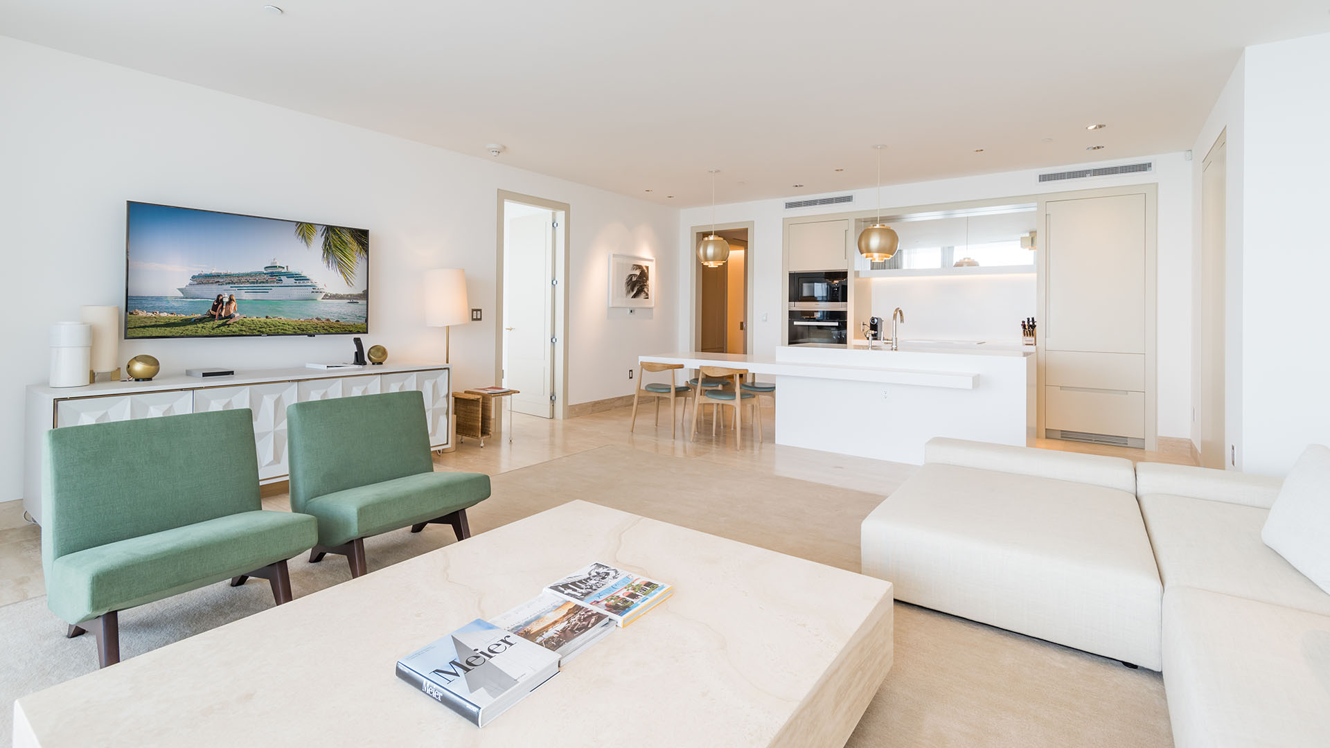Open living room with coastal TV wall, kitchen, and green lounge chairs at The Surf Club Four Seasons, Fort Lauderdale luxury and ultra luxury condos.